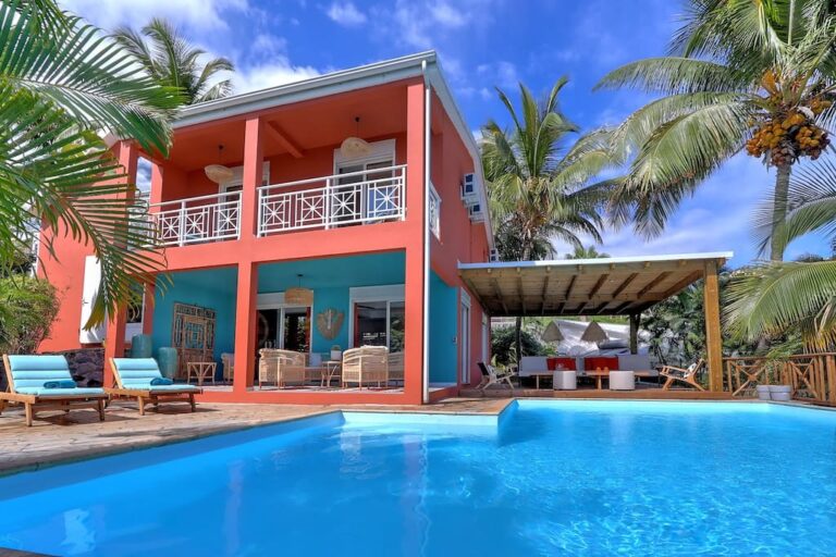 Villa avec piscine et terrasse tropicale bordée de palmiers.